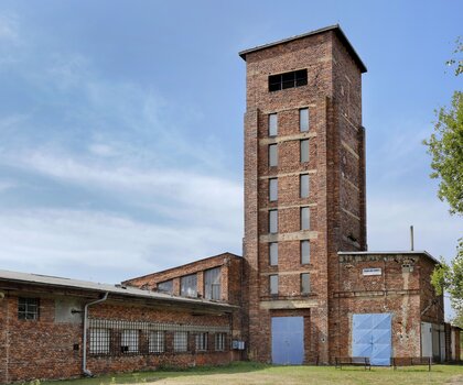 Srpen 2025 pohled na věž ve směru od východu, zamřížovaná okna jsou na kancelářích a laboratořích, kde civilní zaměstnanci zapisovali váhu každého barelu a informace o U rudě